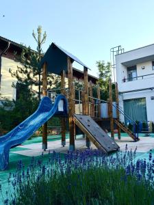 a playground with a slide in a yard with purple flowers at Hotel Vibee Liptov in Liptovský Ján