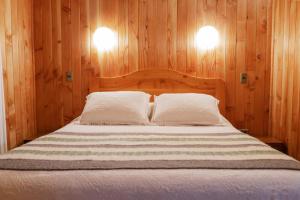 a bedroom with a bed with wooden walls and two lights at Cabañas en neltume in Neltume