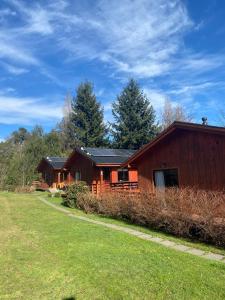 a large wooden house with a grass field next to it at Cabañas en neltume in Neltume
