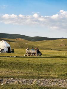a group of people sitting on a bench in a field at Horse Riding Son-kol in Song-Kul