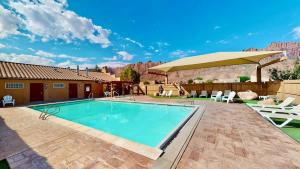 a swimming pool with a patio with chairs and an umbrella at Mountain Paradise #G3 in Moab +20 photos