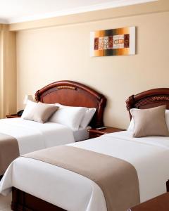 two beds in a hotel room with white sheets at Hotel Raices in Ambato