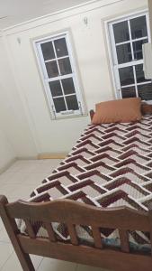 a bed in a white room with two windows at Tiny house in Paramaribo