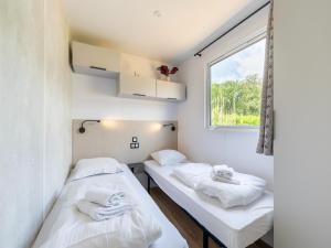 two beds in a small room with a window at Charming caravan with terrace for 6 in Vierhuizen
