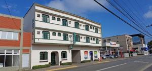 a white building with green shutters on a street at Hotel Bavarium in Joinville