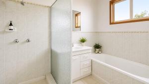 a white bathroom with a tub and a sink at Summer House On Kurrawa - stunning beach views in Kioloa +5 photos