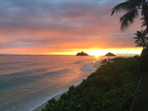 a sunset on a beach with palm trees and the ocean at 5-star Lanikai BEACHFRONT (5 bedrooms,sleeps 13) in Kailua +135 photos