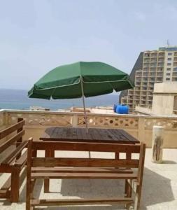 a picnic table with a green umbrella on the beach at Appartement avec terrasse Vu sur mer in Rebaïb