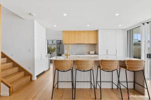 a kitchen with white walls and a counter with bar stools at Waters Edge On Wattle, Absolute Beachfront Luxury in Yeppoon +26 photos