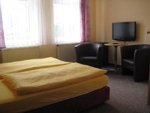 a bedroom with a bed and two chairs and a tv at Hotel Gesellschaftshaus in Bergen auf Rügen