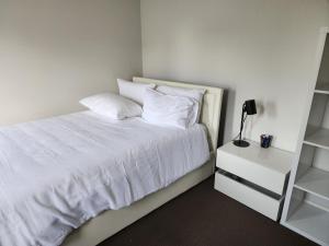 a white bed with white pillows and a night stand at Sunset in Pakenham in Pakenham