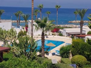 a resort with a pool and palm trees and the ocean at Villa Margo by the Sea in Paphos