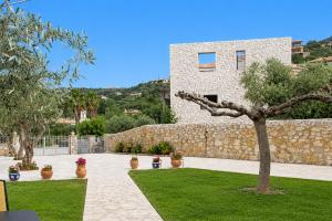 a house with a stone wall and a tree in a yard at Emilia's Guest House with Sea View Balcony, Stoupa in Stoupa