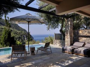 a patio with a bed and an umbrella and chairs at Atlantica Grand Mediterraneo Resort - Adults Only in Kompítsion