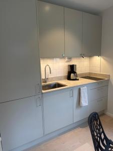 a kitchen with white cabinets and a sink and a chair at Höllviksstugan in Höllviken