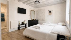 a white bedroom with two beds and a television at Grand appart 6 pers Cœur de Nemours in Nemours