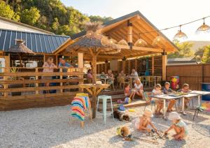 a group of children sitting in the sand in front of a restaurant at Camping Hôtel Maui in Tournon-sur-Rhône