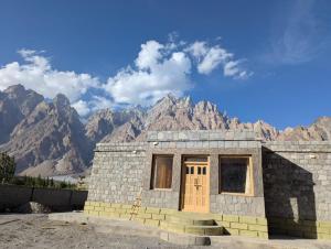 a stone building with a door in front of mountains at Passu Didargah Resort in Pasu