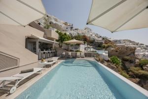a pool with chairs and umbrellas next to a house at Mancave Sanctum Caldera Suites in Oia