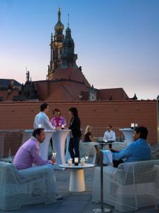 
three people sitting at a table in front of a clock tower at Hyperion Hotel Dresden Am Schloss in Dresden
