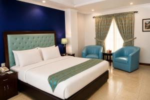 a bedroom with a bed and two blue chairs at Royalton Hotel Rawalpindi in Rawalpindi +34 photos