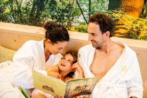 a man and woman reading a book to a child in a bath tub at Das Bayrischzell Familotel Oberbayern in Bayrischzell