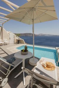 a table and chairs with an umbrella next to a swimming pool at Mancave Sanctum Caldera Suites in Oia