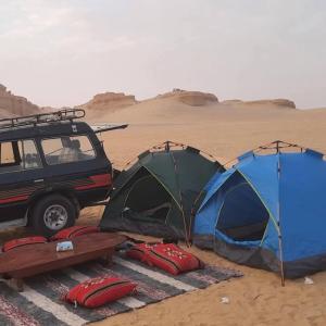 two tents in the sand next to a jeep in the desert at Fayoum Safari Camp in Qaryat at Ta‘mīr as Siyāḩīyah