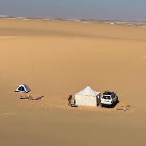a person standing next to a tent and a car on a beach at Fayoum Safari Camp in Qaryat at Ta‘mīr as Siyāḩīyah