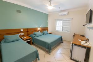 a hotel room with two beds and a television at Hotel Nova York in Araçatuba