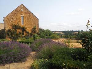 an old brick building with purple plants in front of it at Hobbs Hole Cottage in Great Tew