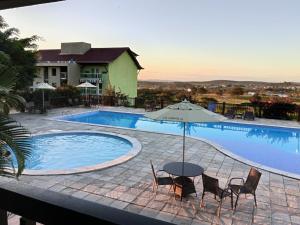 a pool with a table and chairs and an umbrella at Flat em Gravatá -Villa Monte Castelo - 2 quartos- Ao Lado da Área de Lazer e das piscinas in Gravatá