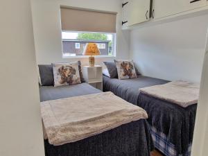 two beds in a small room with a window at 67 Broadside Holiday Chalet near Broads & Beaches in Stalham