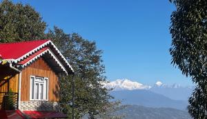 a house with a red roof with mountains in the background at Chyajalo homestay in Darjeeling