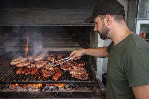 a man cooking sausages and meat on a grill at Hotel Casa De Campo in Santa Cruz