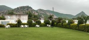 a lawn with white tables and chairs in front of a building at Sariska Celebration Hotel & Resort in Alwar
