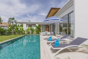 a swimming pool with chairs and an umbrella next to a house at Luxury 3-Bedroom private pool villa Trichada Breeze in Phuket
