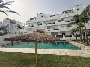 a straw umbrella in front of a large building at Apartamento Golf Valle Romano in Estepona