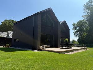 a black house with a deck in the grass at Stodoły Północ in Debina
