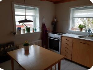 a kitchen with a table and a stove and two windows at Central apartment in Vestmanna in Vestmanna