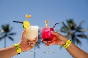 two people holding cocktails in their hands with palm trees in the background at El Aram Beach Cabo - All Inclusive in Cabo de Santo Agostinho