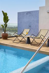 two chairs and a table next to a swimming pool at NH Luz Huelva in Huelva