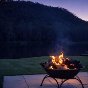 a fire pit sitting on a patio next to a lake at The River House - Wisemans Ferry in Wisemans Ferry