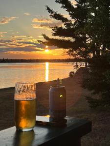 a glass of beer sitting on a table with the sunset at Bob's Cabin at Wishart's Point Lodge in Neguac +3 photos