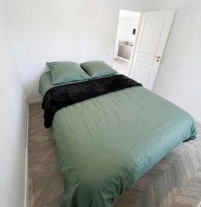 a bed in a white room with a green comforter at Cosy appartement in Miniac-Morvan
