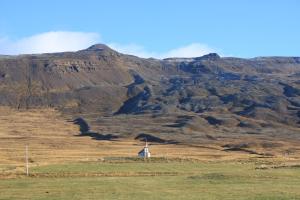 a church in a field with a mountain in the background at Hofsstadir Farmhouse in Hofstaðir