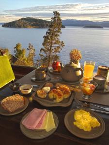 a table topped with plates of breakfast foods and a view of the water at Hosteria Santa Rita in San Carlos de Bariloche