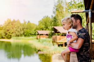 a man holding a little girl sitting on a post next to a lake at Forest Cube 5 persons #702 in Maasbree
