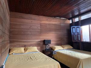 two beds in a room with wooden walls at Hotel bar y restaurante Millenium Lanquin in Lanquín