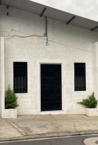 a white building with a black door and three windows at Mini Loft en Quezaltepeque in Quezaltepeque